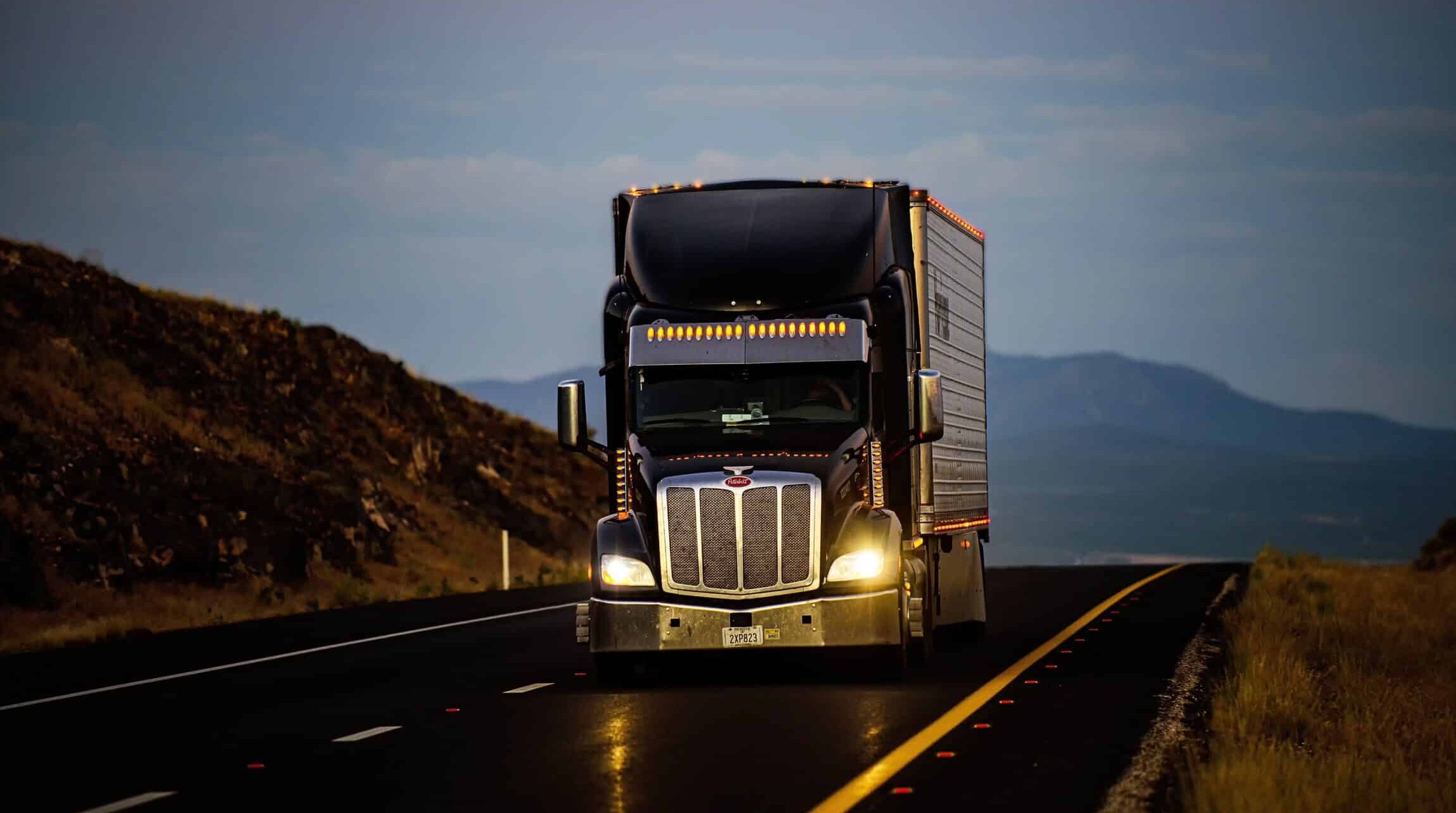 A truck with the headlights on driving on a highway at dusk