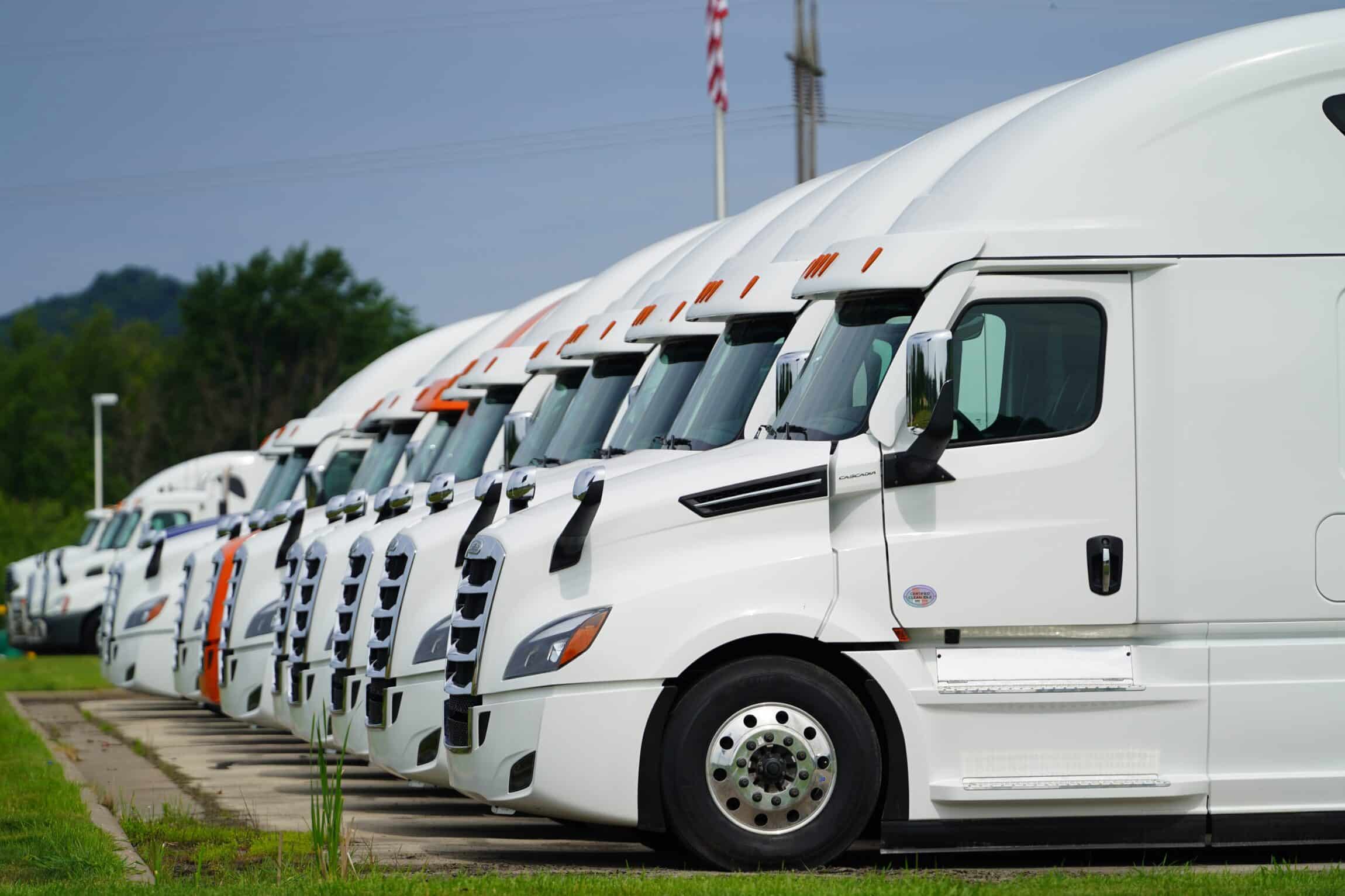 A row of white semi-trucks is neatly parked side by side in a lot