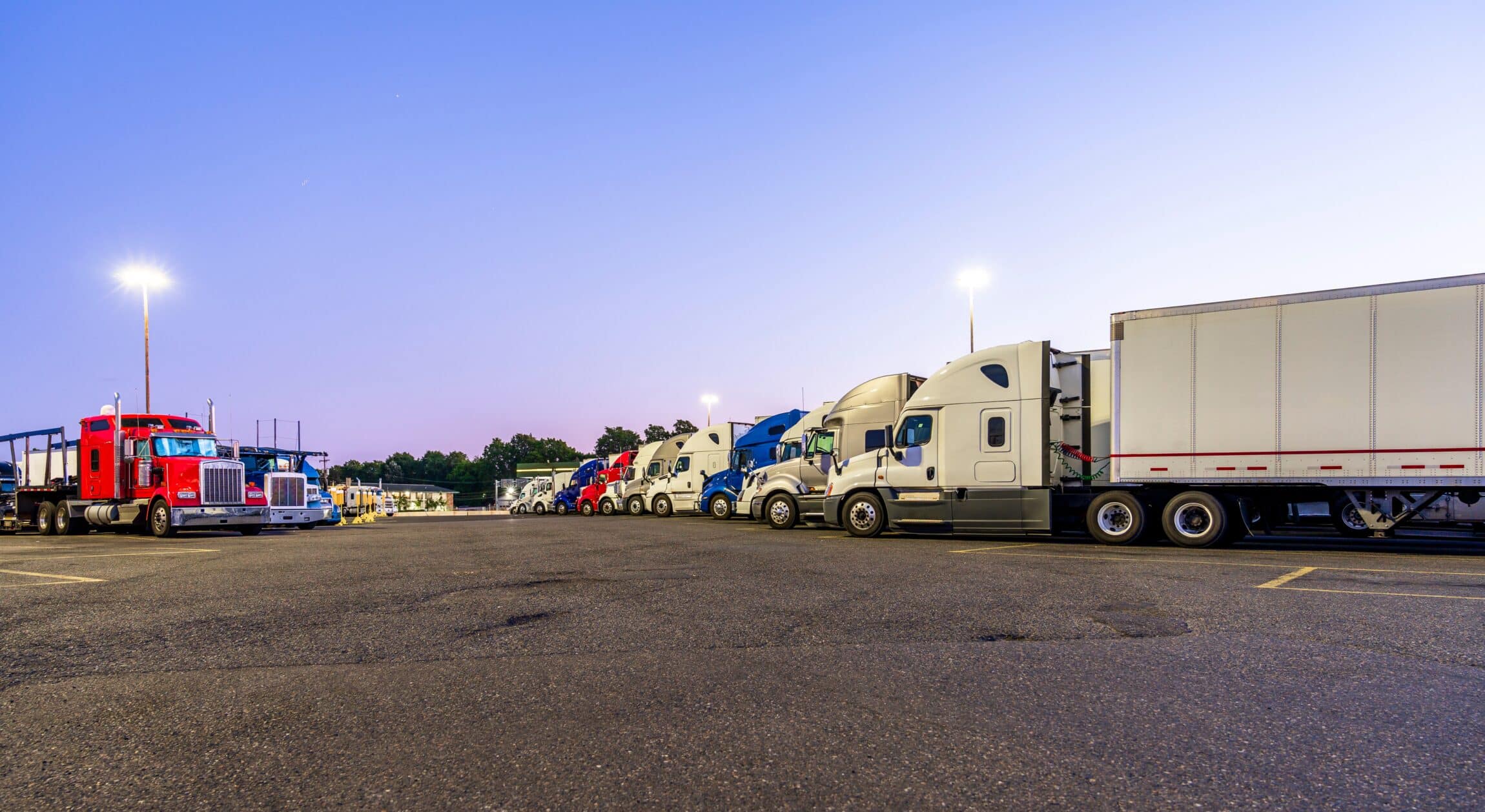 big rigs semi trucks with semi trailers standing in row on truck stop parking lot