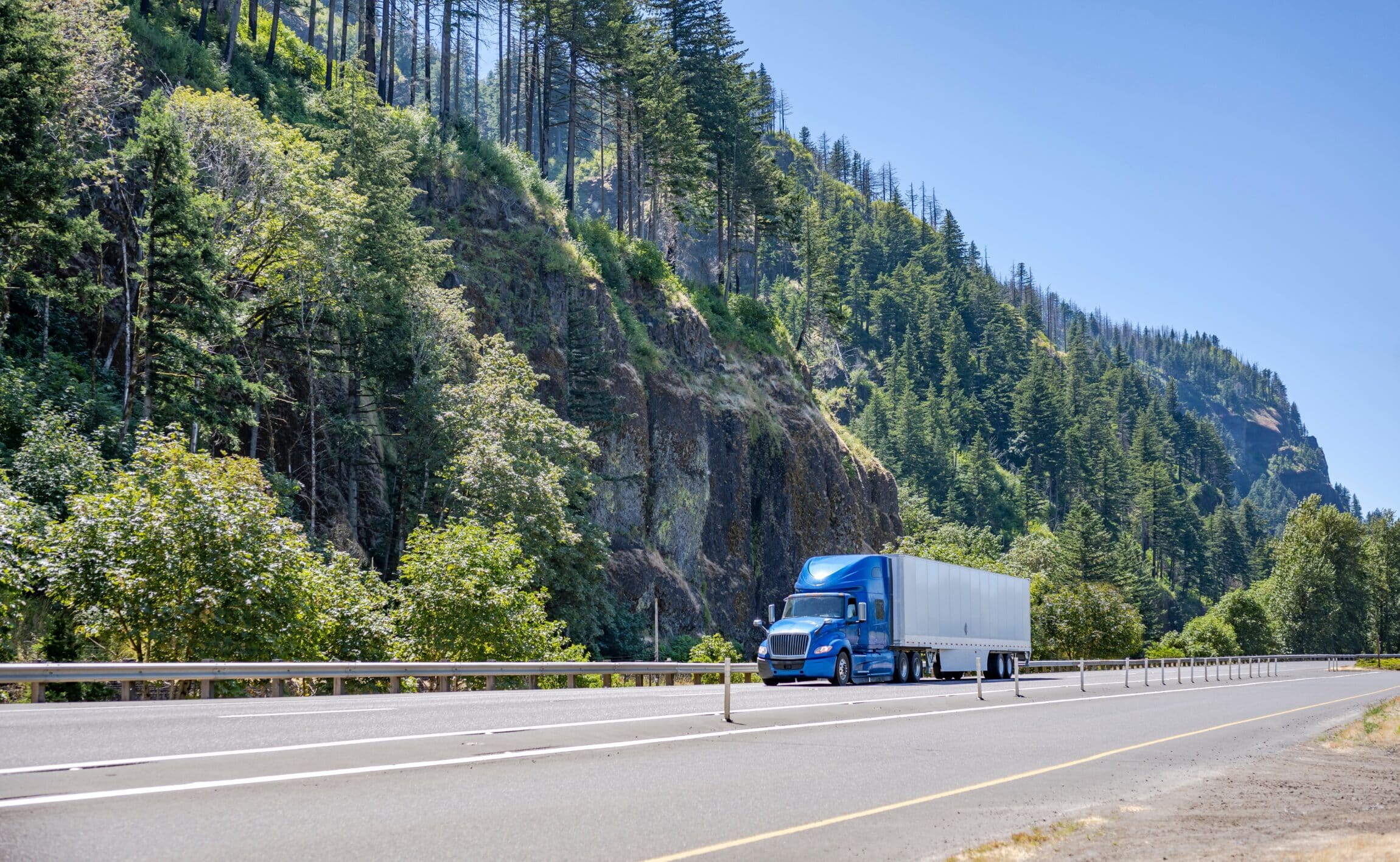 Blue industrial big rig semi truck running on summer highway