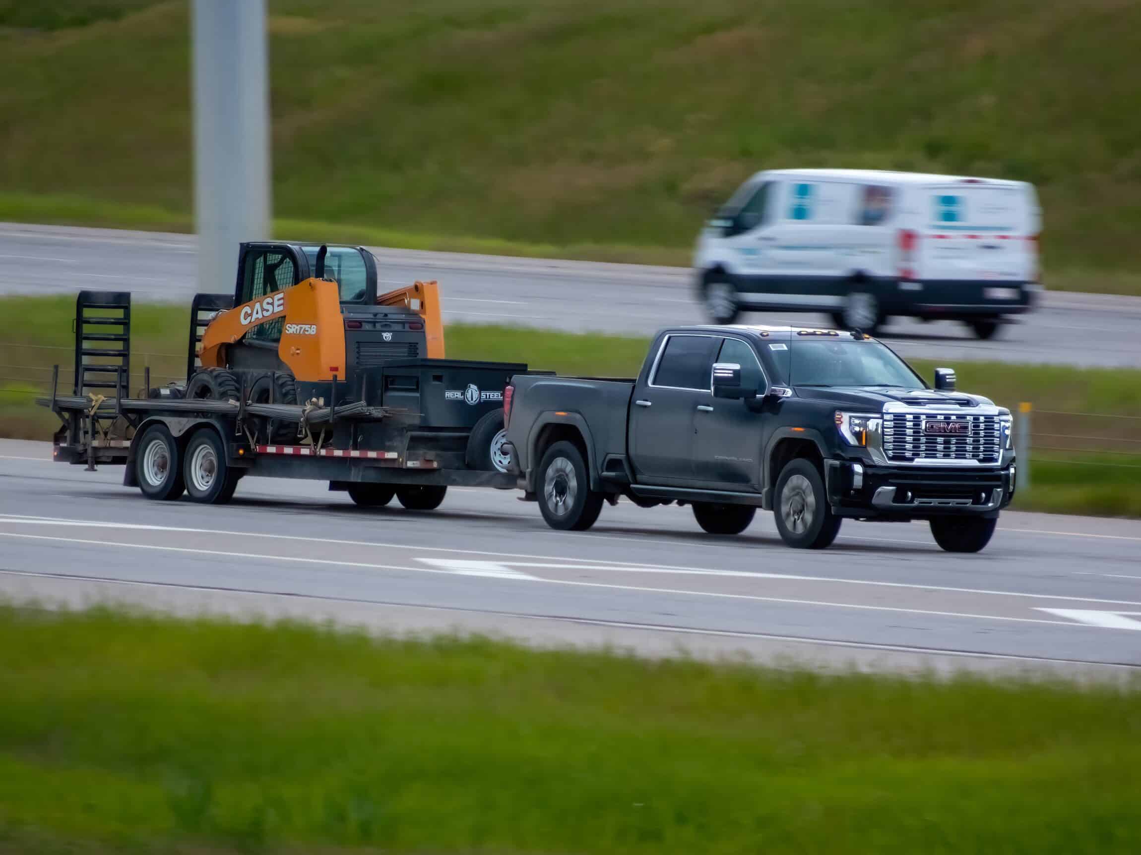 pickup truck tows a black trailer carrying a construction backhoe machine