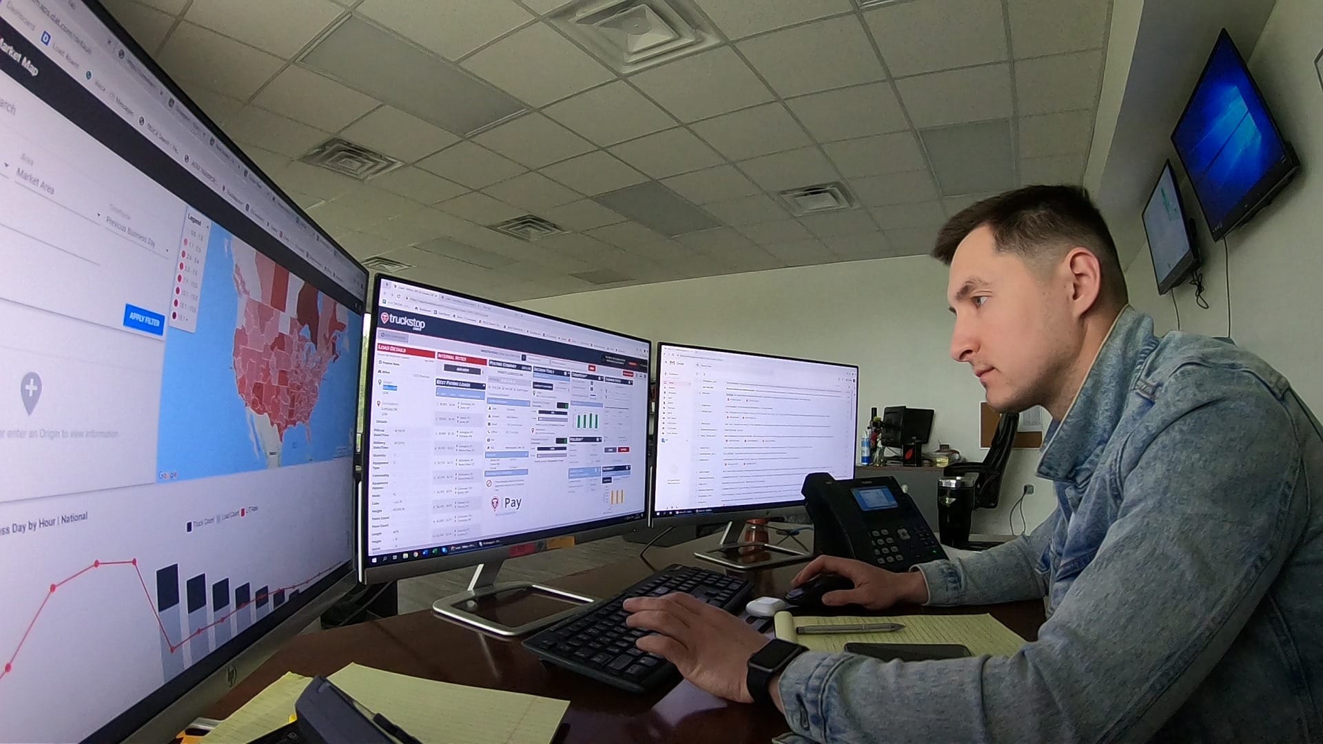 Logistics dispatcher working at a desk with three large computer monitors displaying tracking software