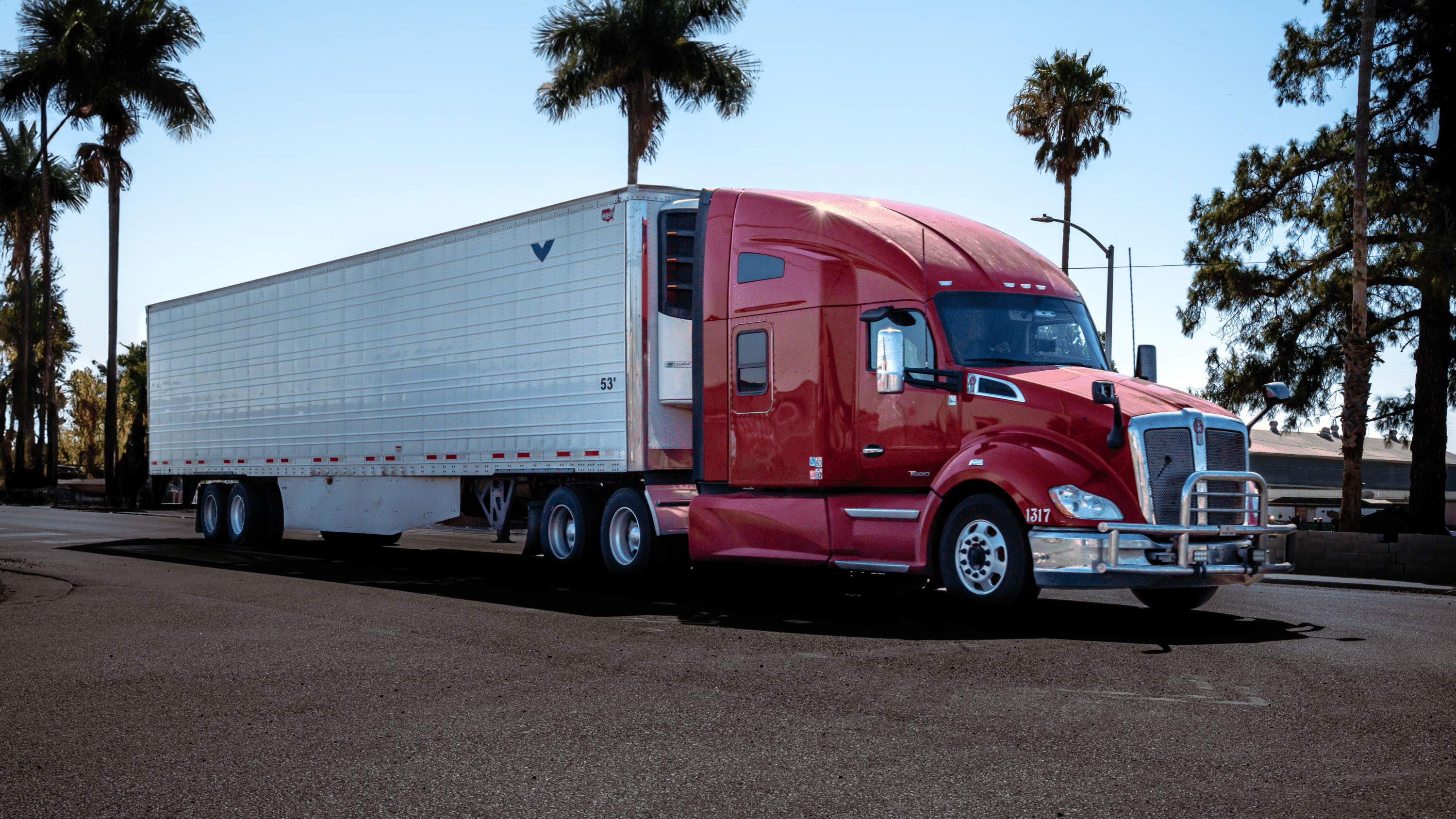 Red bonnet semi truck standing in front of the palms