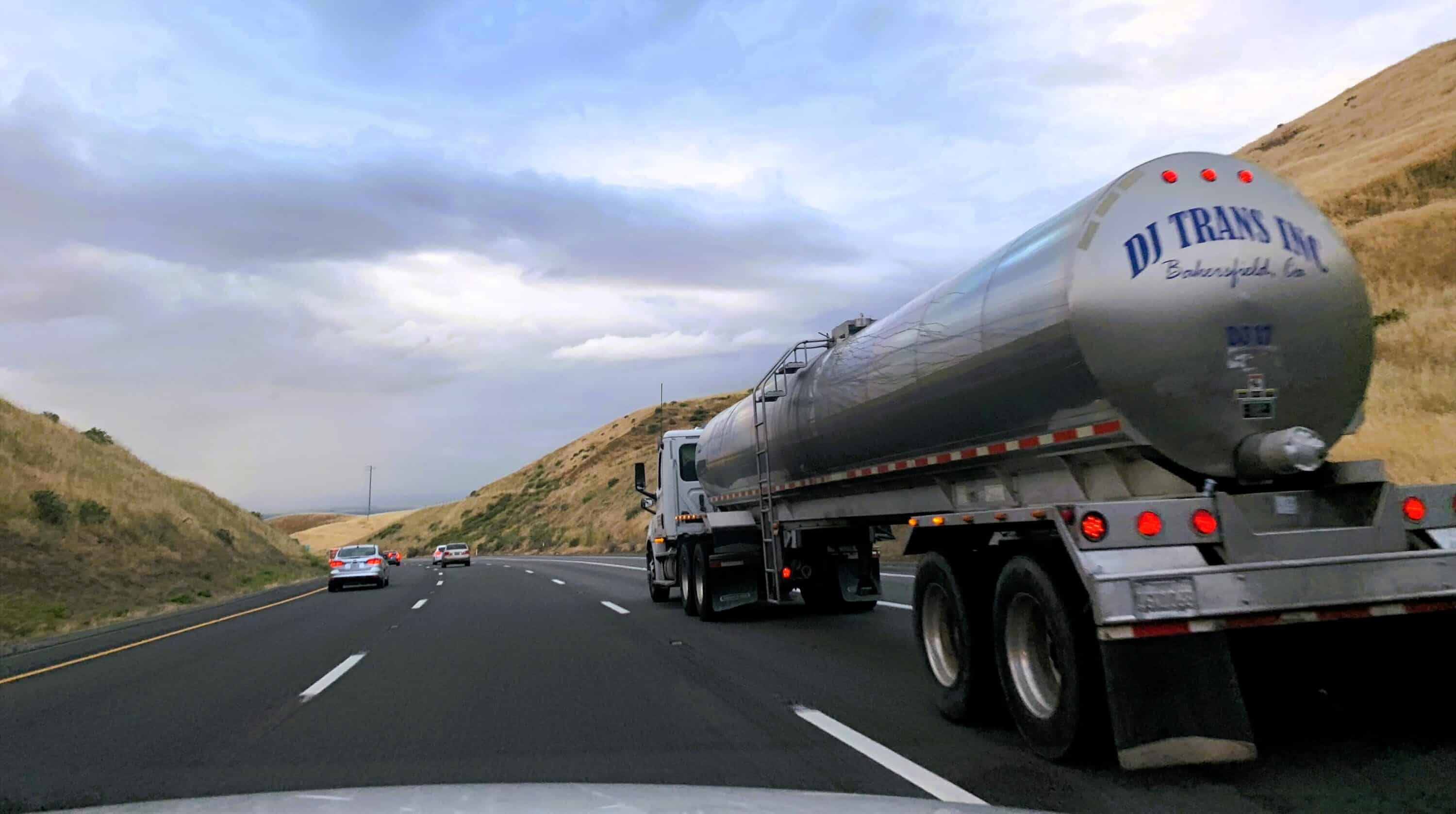 Tanker truck transporting liquid cargo on a multi-lane highway between hills and open terrain