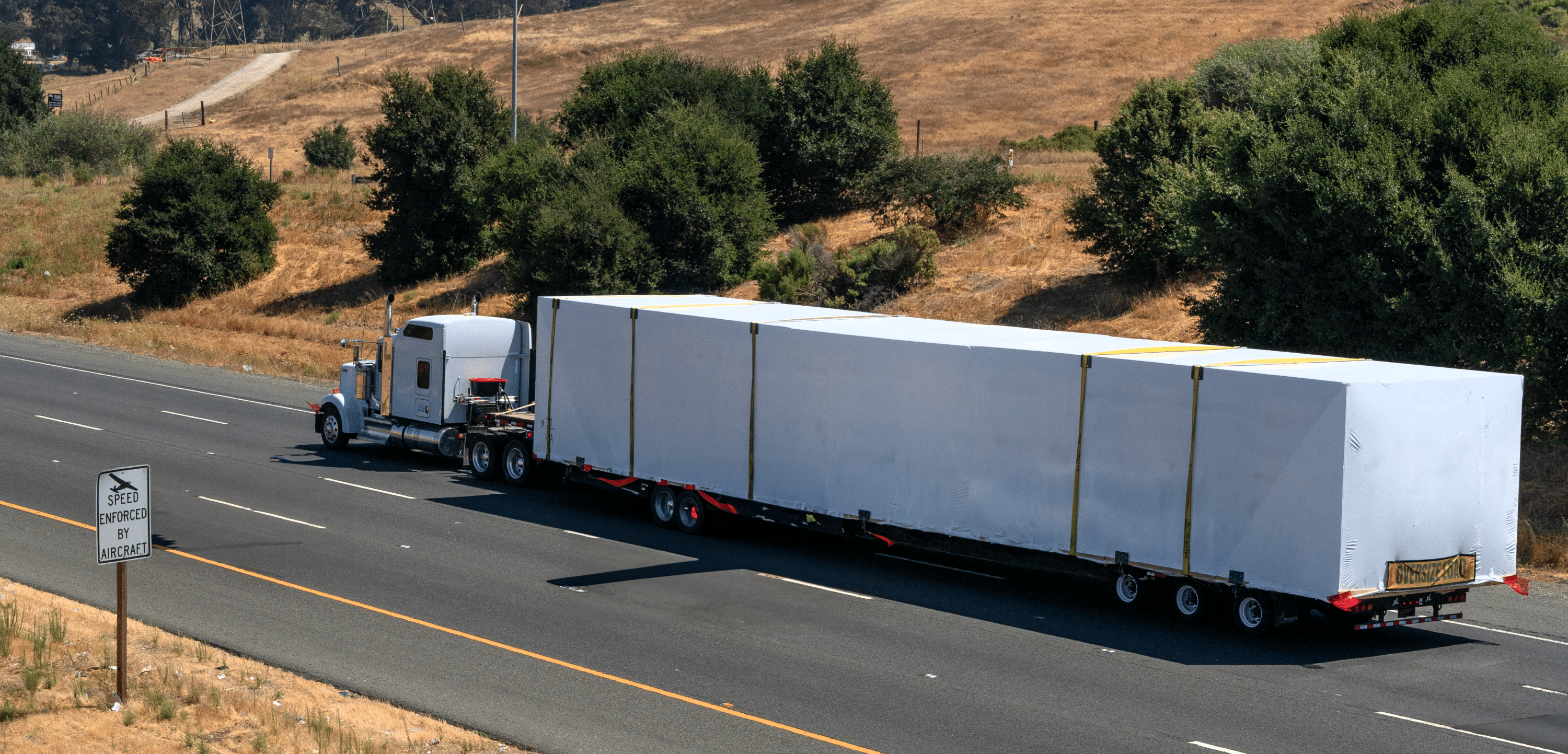Semi-truck hauling an oversized load on a highway through a rural landscape