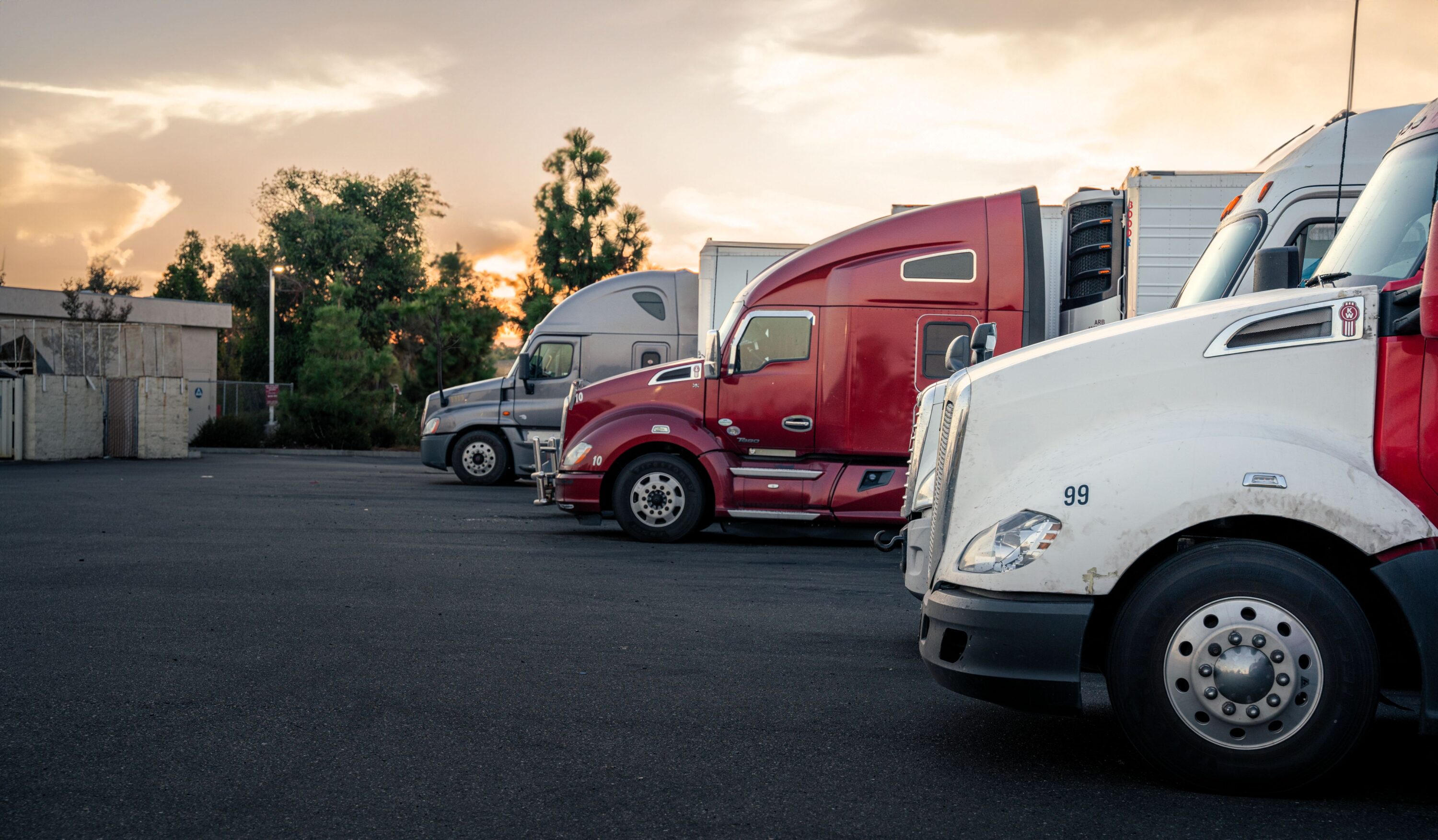 Commercial semi-trucks parked in a truck stop lot at sunset
