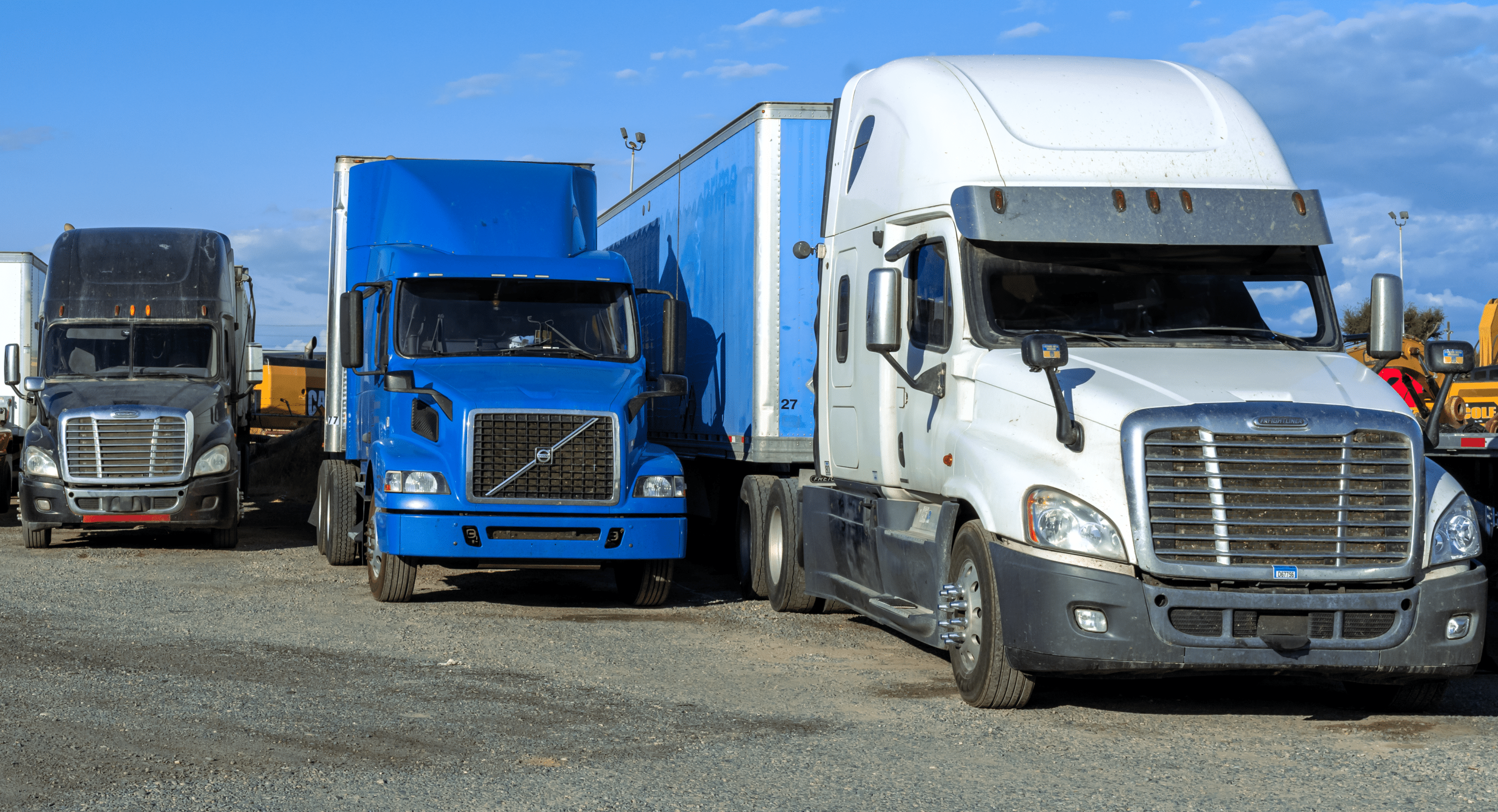 Three semi-trucks parked side by side in a commercial vehicle yard