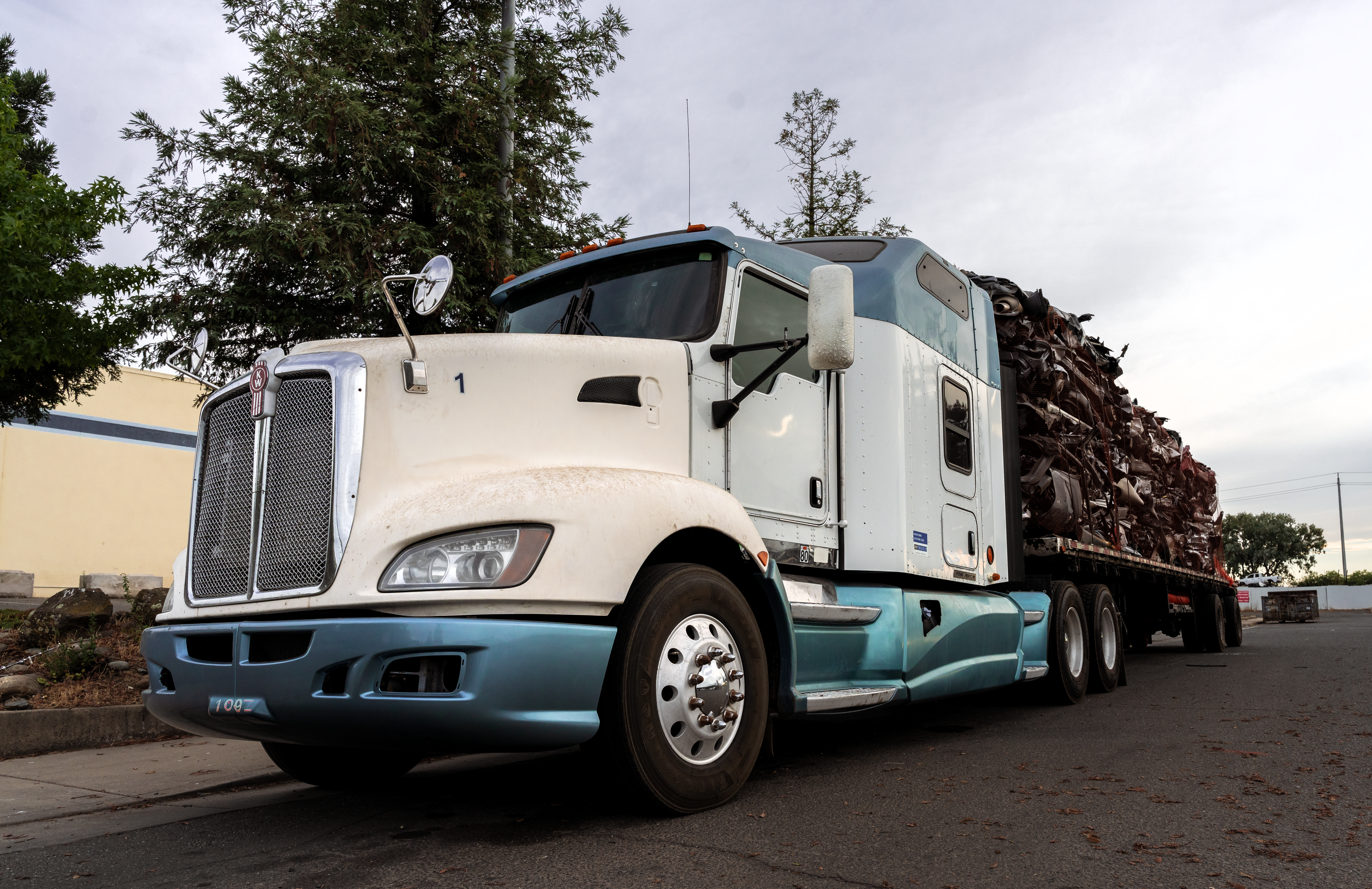 White semi-truck hauling a flatbed trailer loaded with scrap metal on an industrial roadway
