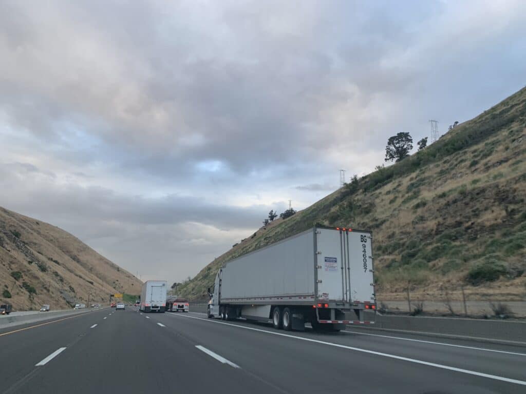 semi driving between mountains under a cloudy sky