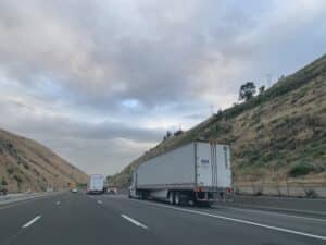 semi driving between mountains under a cloudy sky