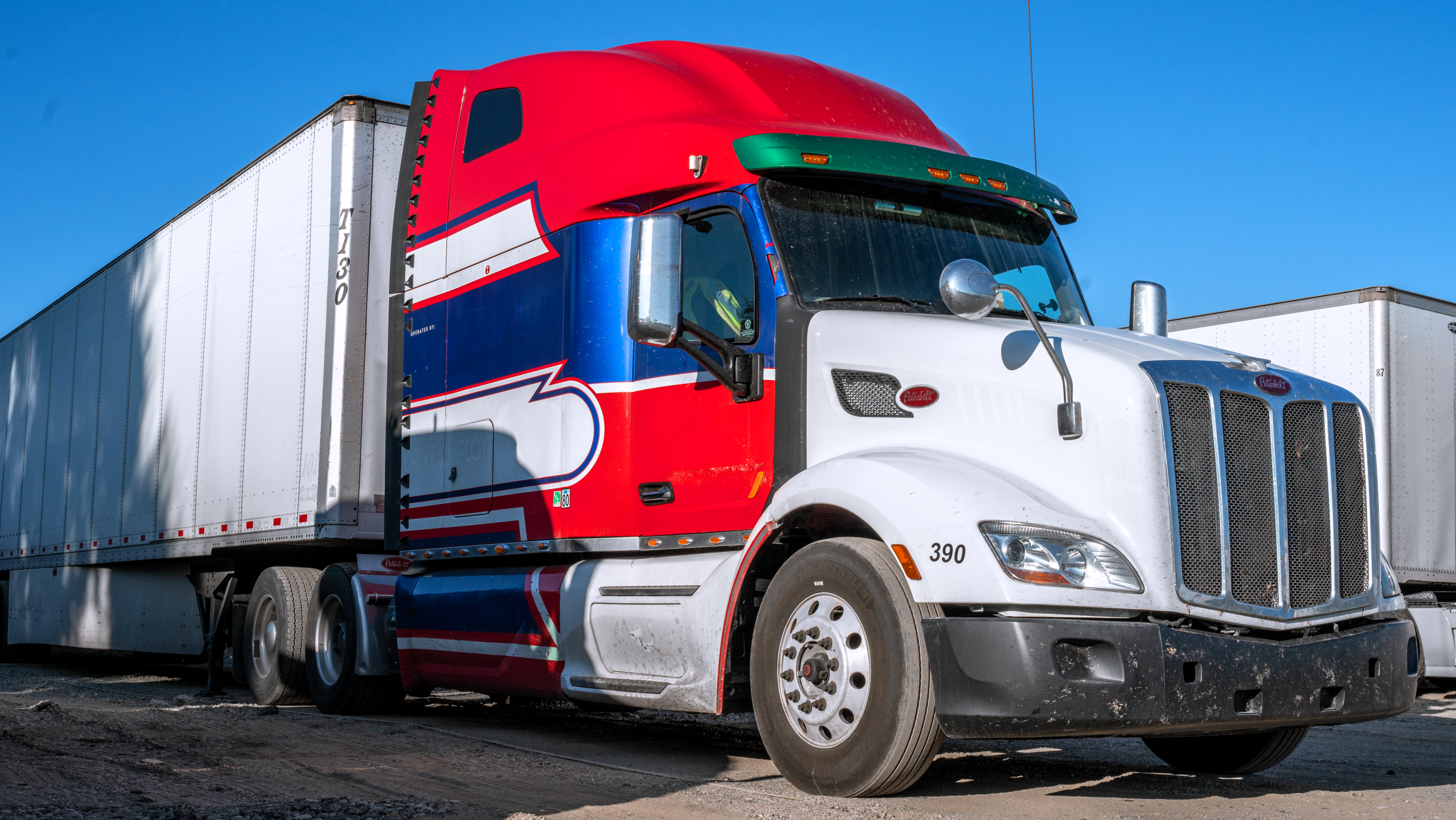 Red and white semi-truck with dry van trailer parked in a commercial truck yard