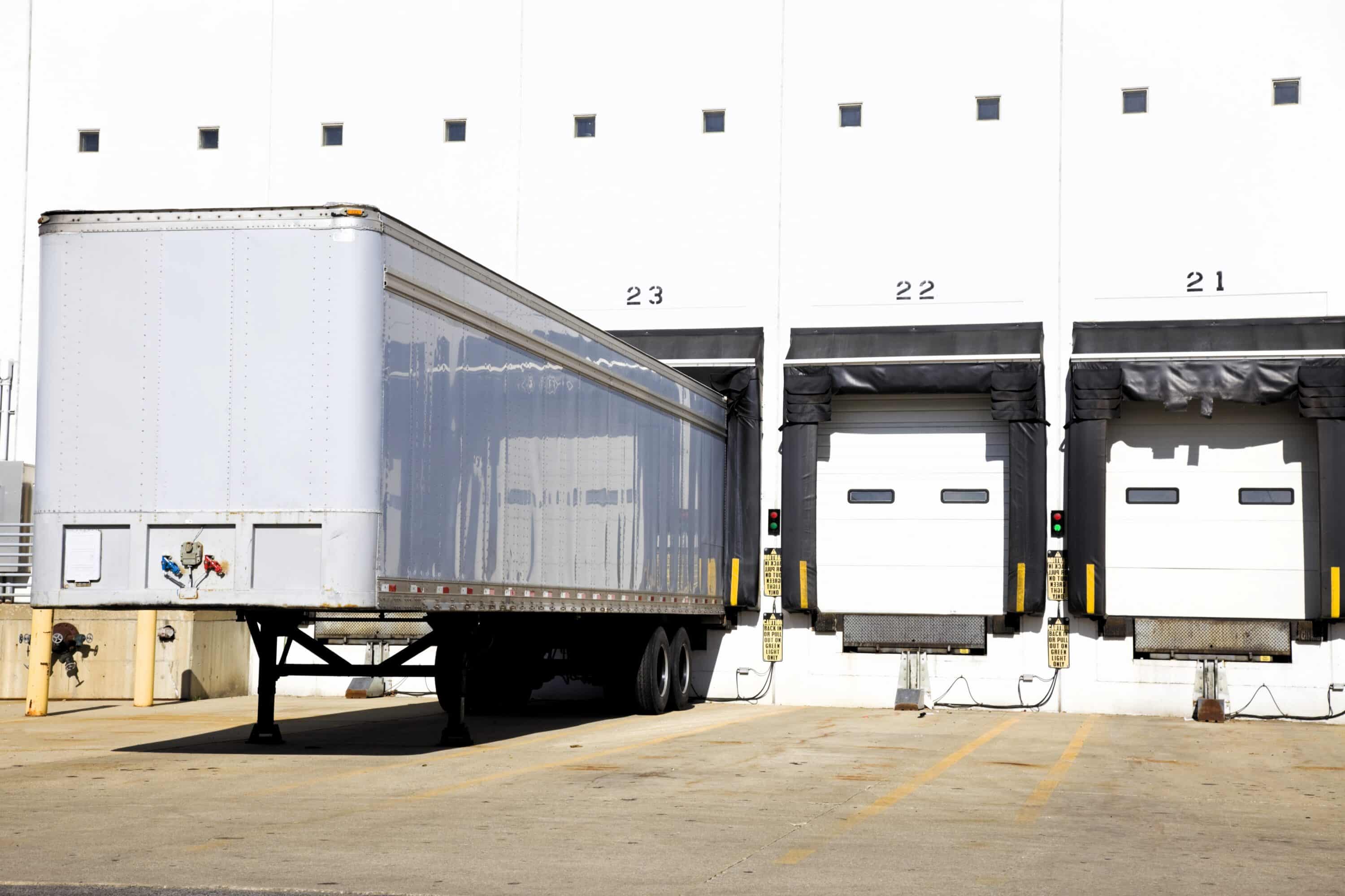 Semi-trailer positioned at a warehouse loading dock beside multiple dock doors