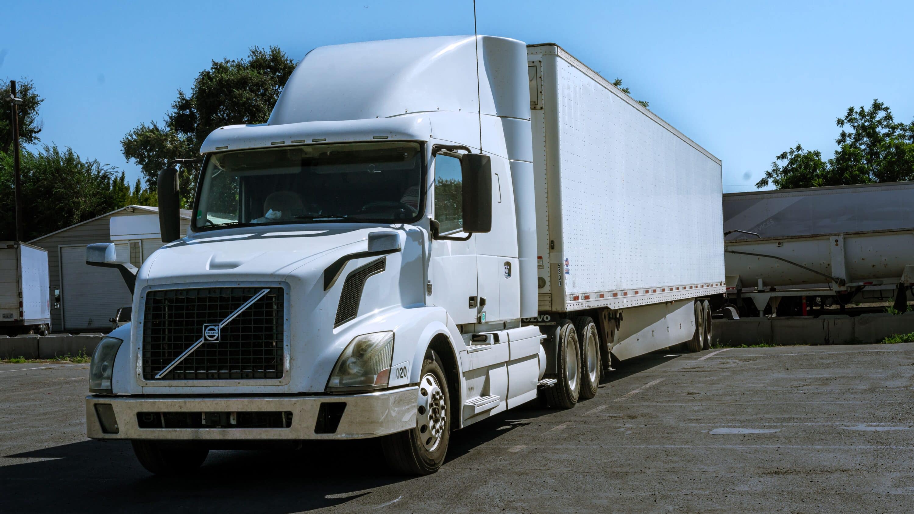White Volvo semi-truck with box trailer parked in a commercial yard