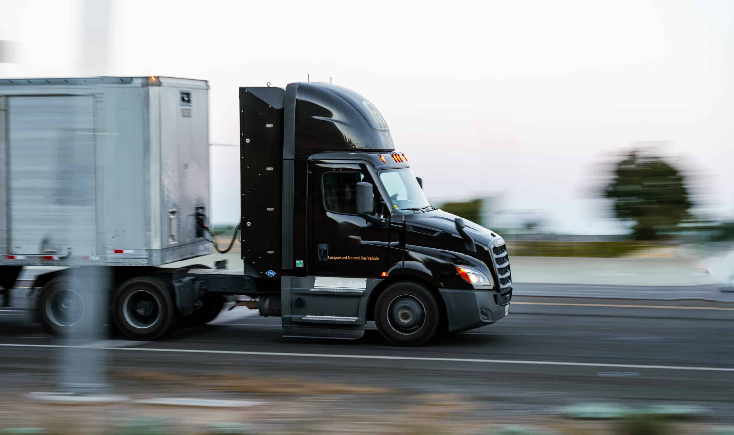 Black semi-truck hauling a box trailer while driving on a highway