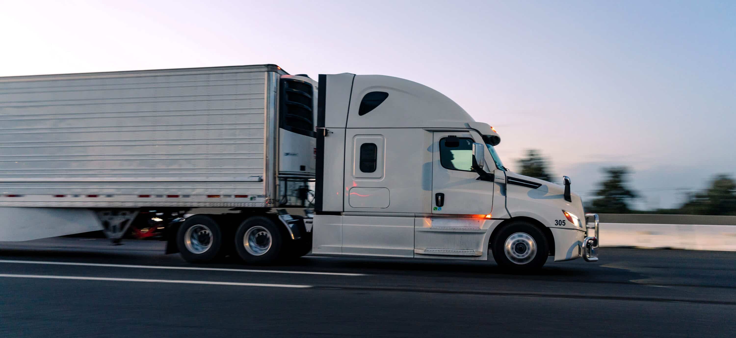 White semi-truck hauling a refrigerated trailer while driving on a highway at dusk