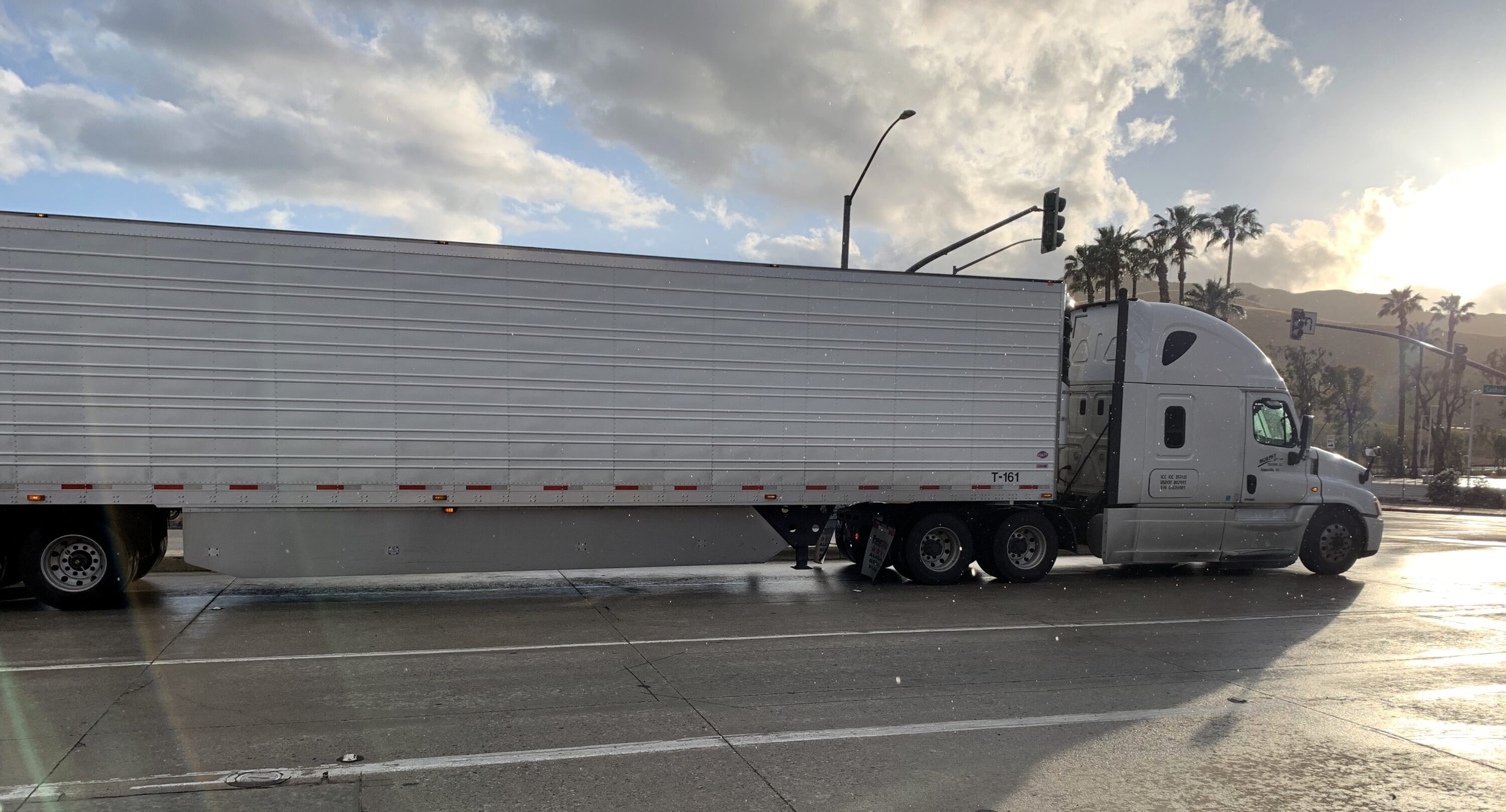 White semi-truck hauling a box trailer through an intersection on a wet roadway