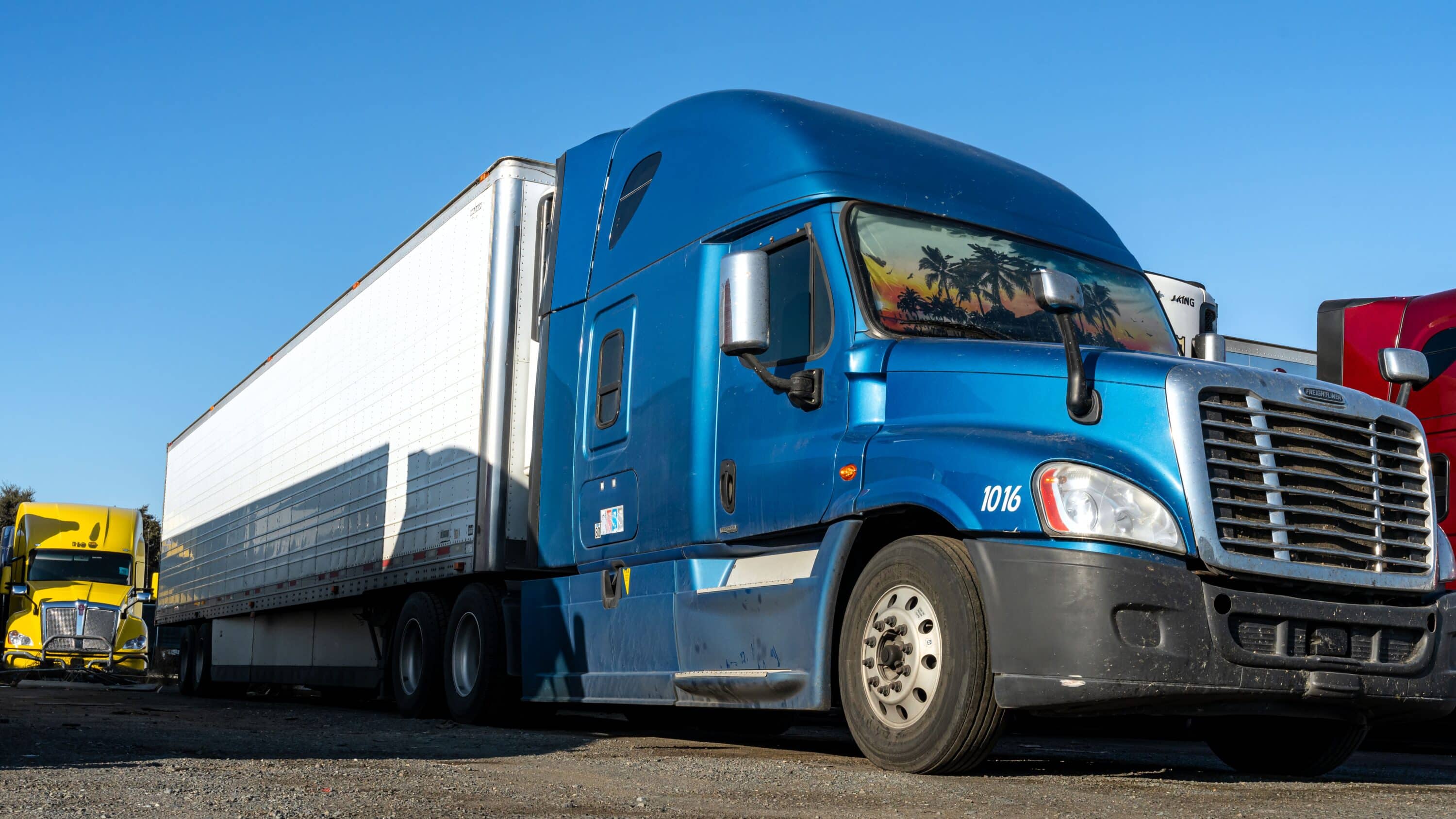 Blue semi-truck with refrigerated trailer parked in a commercial truck lot