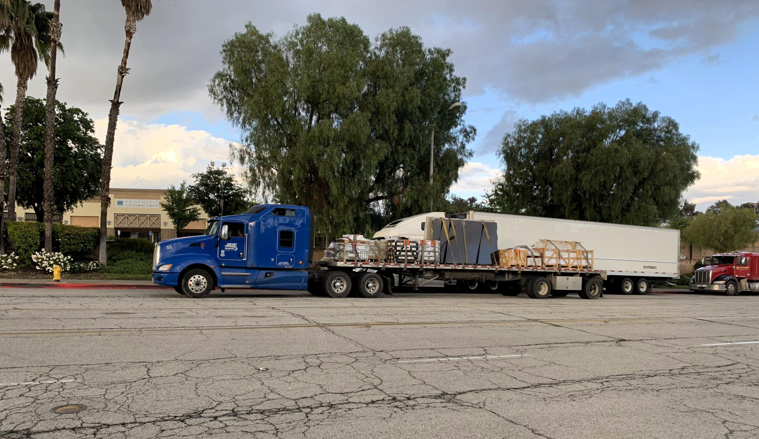 Blue semi-truck hauling a flatbed trailer loaded with cargo on a city street