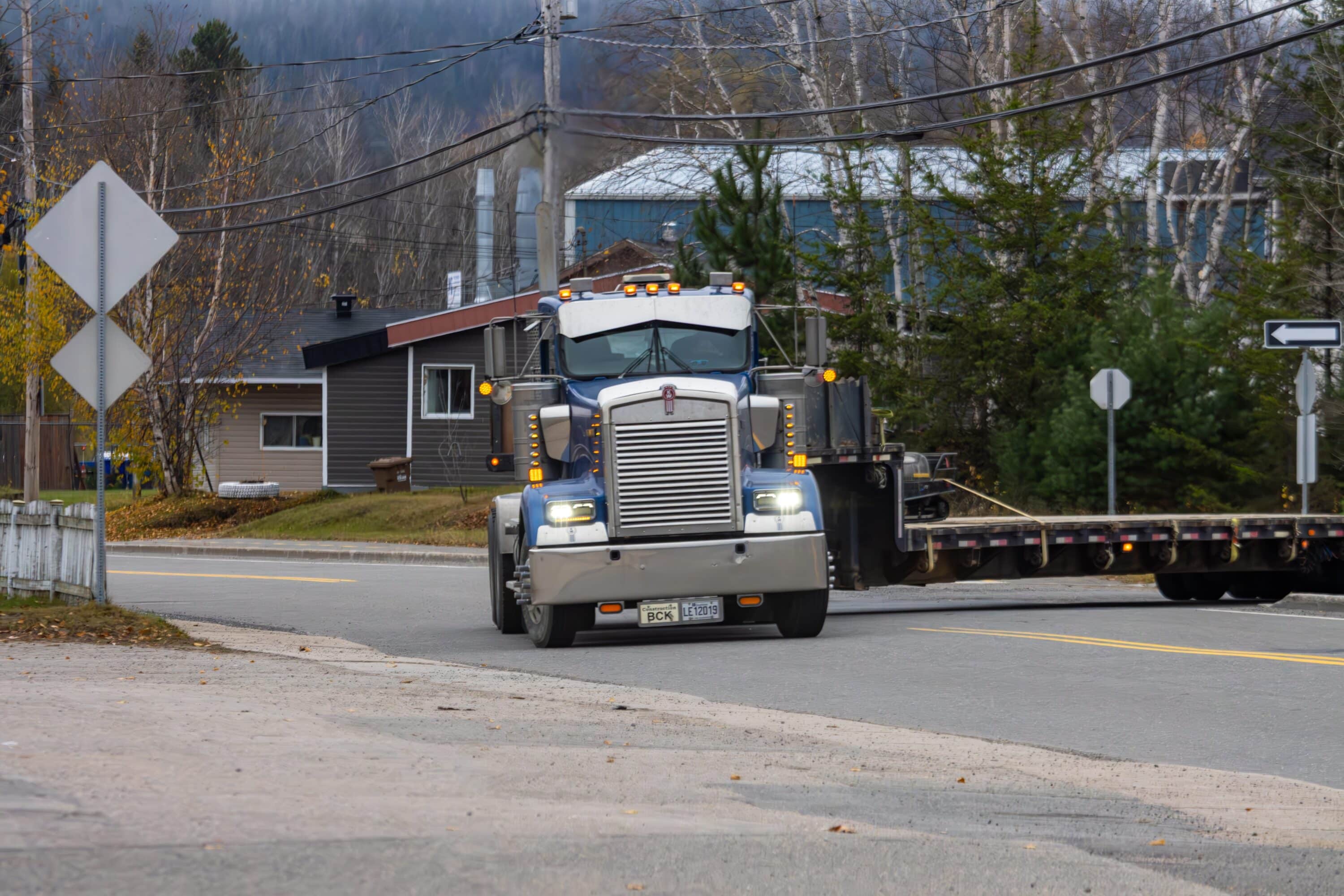 Gray semi-truck pulling a flatbed trailer through a small town intersection