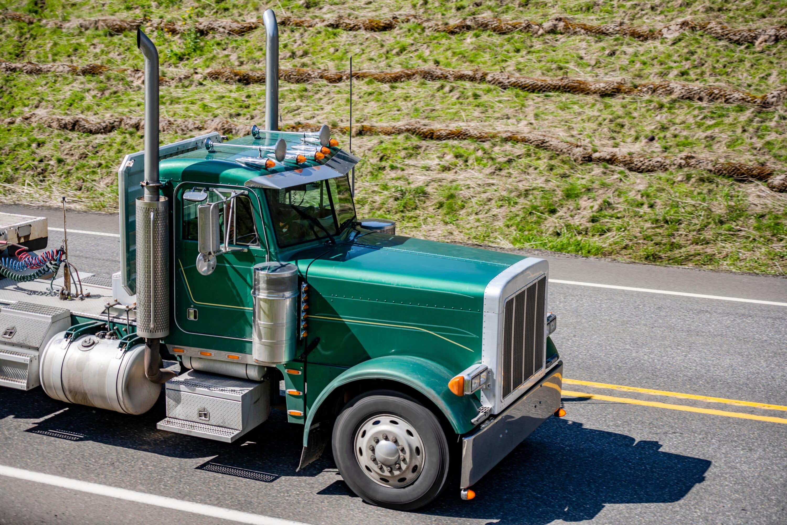 Green semi-truck tractor traveling on a paved roadway viewed from above