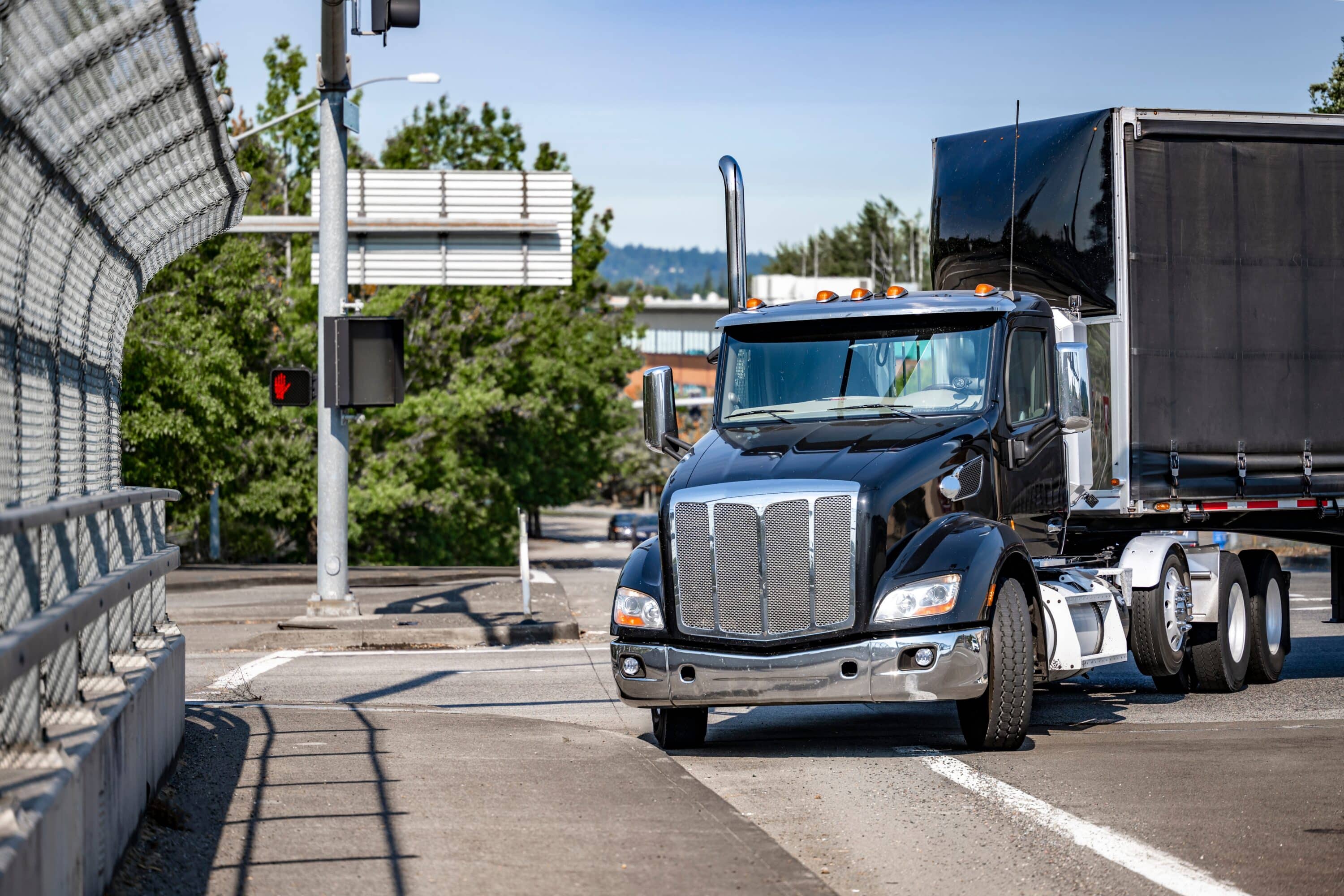 Black semi-truck hauling a trailer on an urban roadway near an overpass