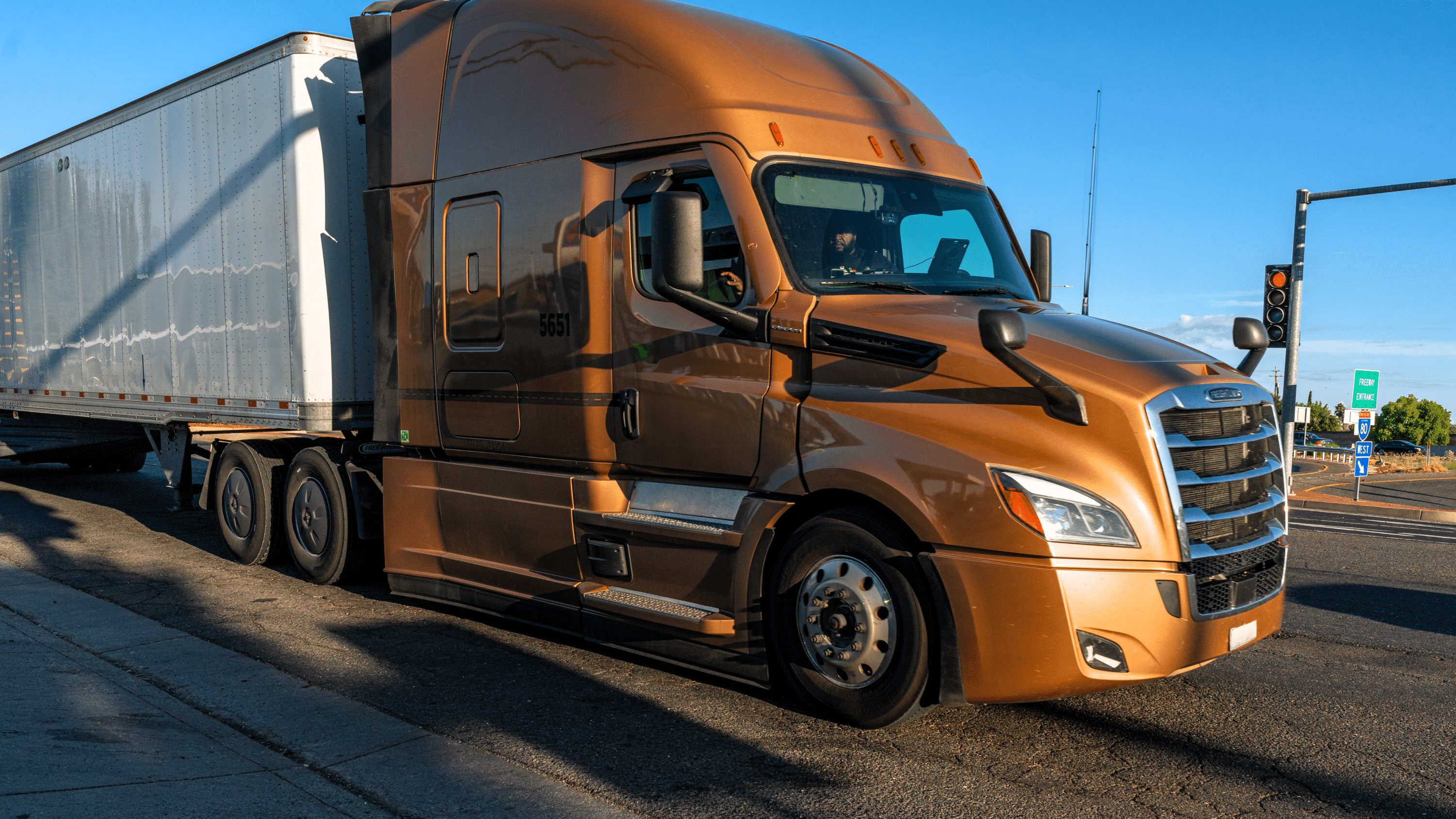 Brown semi-truck hauling a box trailer stopped at a traffic light intersection