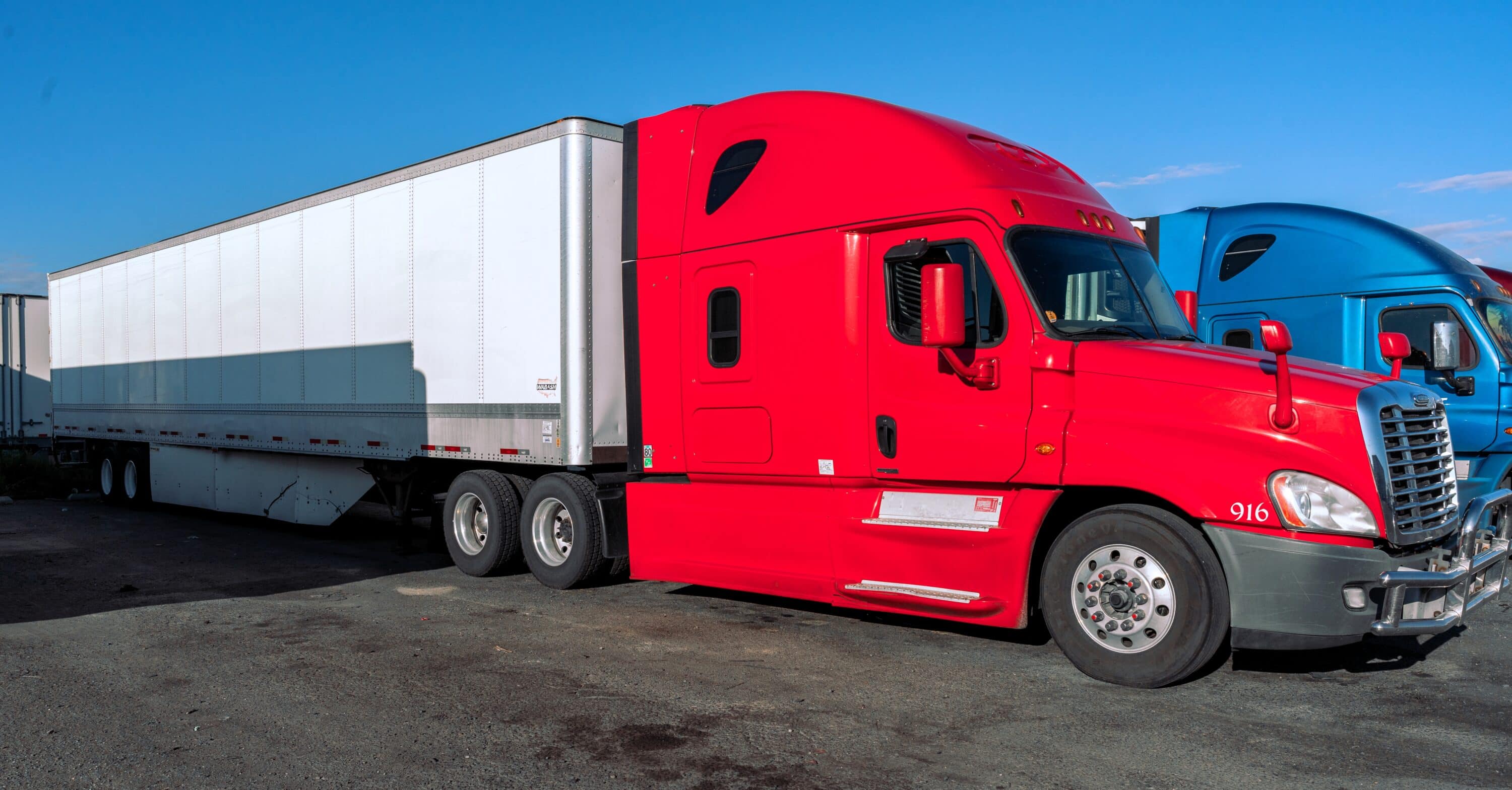 Red semi-truck with box trailer parked in a commercial truck lot
