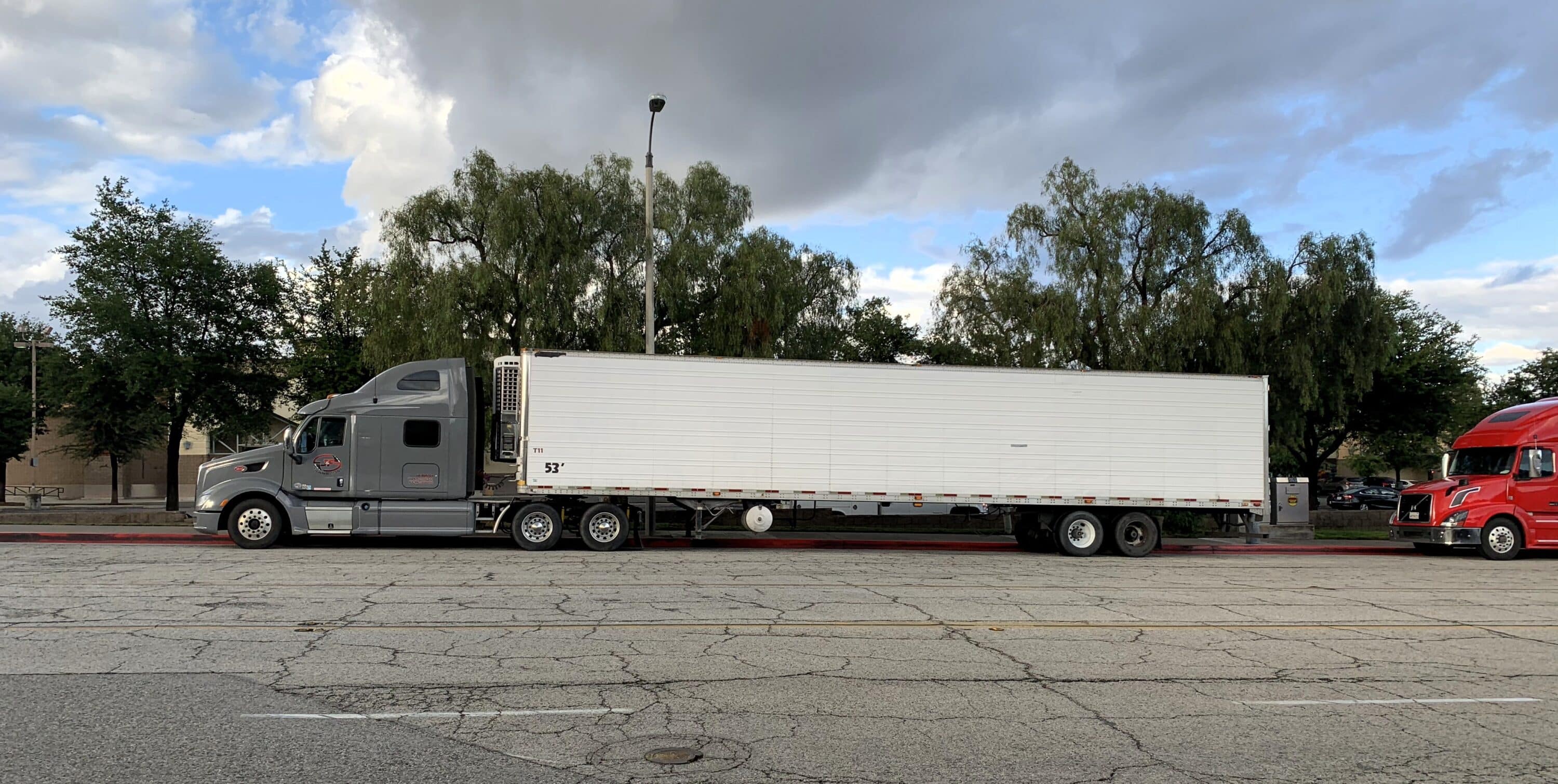 Gray semi-truck hauling a long box trailer parked along a city street
